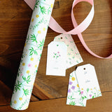 Floral-patterned gift wrap and tags on a wooden surface with a pink ribbon.
